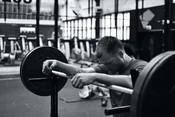 Man looking sad standing next to a barbell in a gym